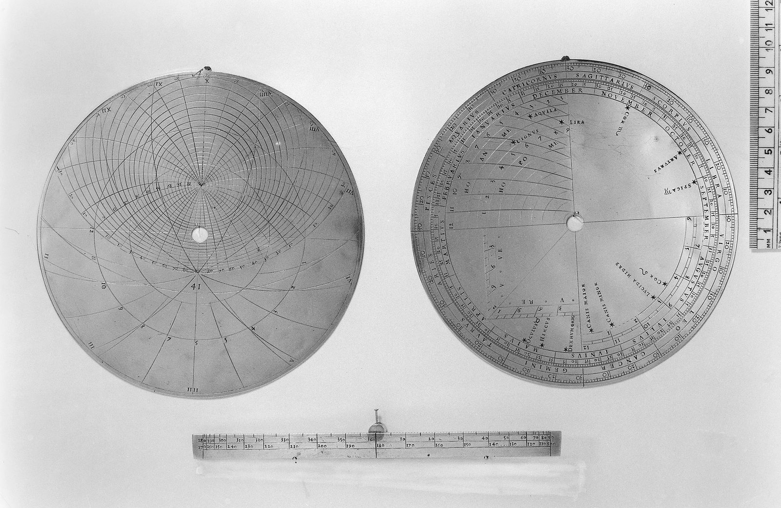 A black and white museum photograph of a circular metal astrolabe plate lying on a plain pale ground. Its face is engraved with a dense net of fine lines: nested arcs crowding towards a point above the centre, curved lines fanning out from a point below it, a long shallow arc running across the middle, and numbered hour lines across the lower half. Roman numerals run round the rim, small numerals label the arcs, and the number 41 is cut into the plate below the centre. A hole pierces the middle and a small tab projects at the top.