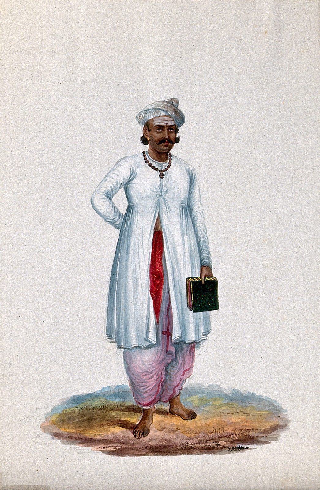 A nineteenth-century Indian gouache painting on a plain cream sheet. A barefoot man stands alone, facing forward, in a long white muslin coat open over a red sash and a pink dhoti, with a white turban, a dark bead necklace and a moustache. His left hand rests behind his hip; in his lowered right hand he holds a small green bound book with gilt edges. He stands on a small oval patch of scrubby brown and yellow ground, and the rest of the paper is empty.