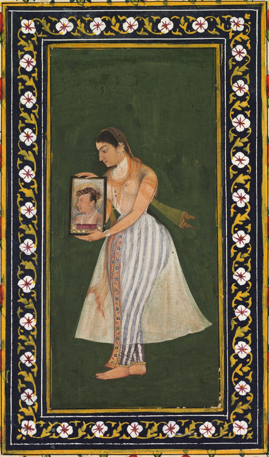 A tall, narrow Mughal painting mounted on a larger album page. A richly dressed woman stands alone in profile, holding up a small rectangular portrait of the emperor Jahangir: an older man with a greying beard, shown from the waist up behind the patterned carpet that marks a palace audience window.