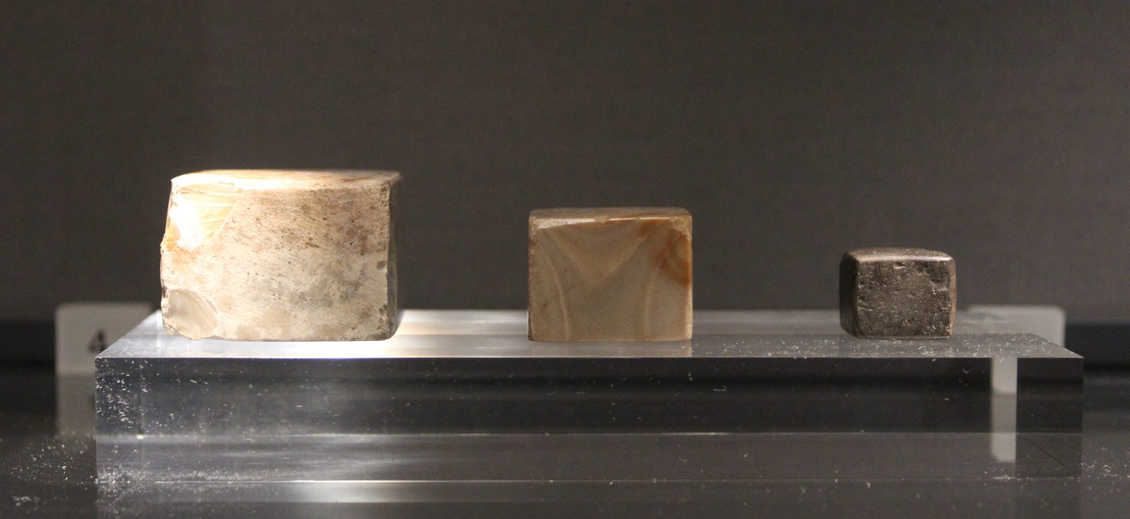 Three small weights from Mohenjo-daro set side by side: plain cubes of chert, a hard dull-coloured stone, with flat squared faces. Mature Harappan period, now in the Ashmolean Museum.