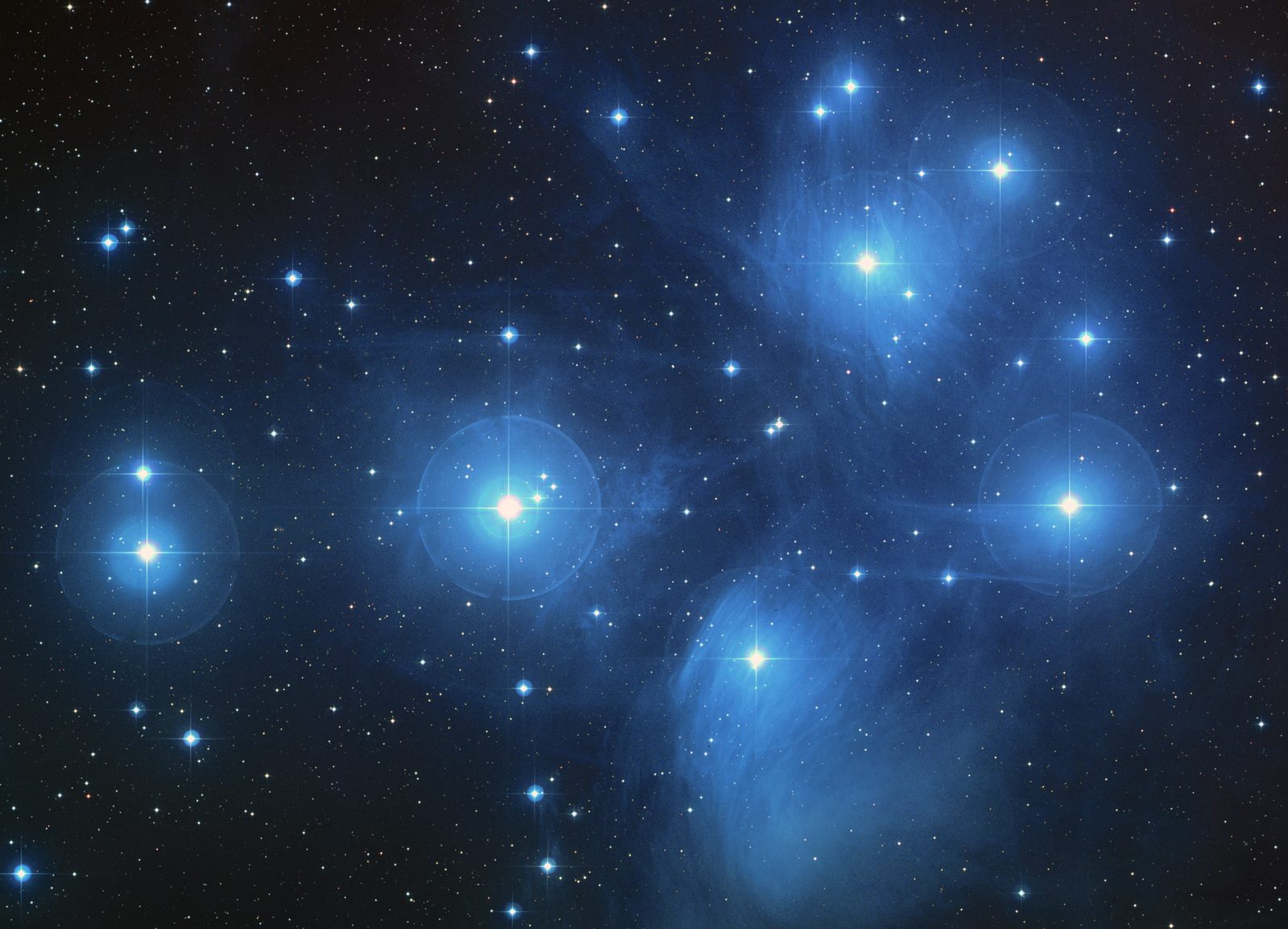 A colour photograph of the Pleiades: six or seven brilliant blue-white stars with four-pointed diffraction spikes, arran