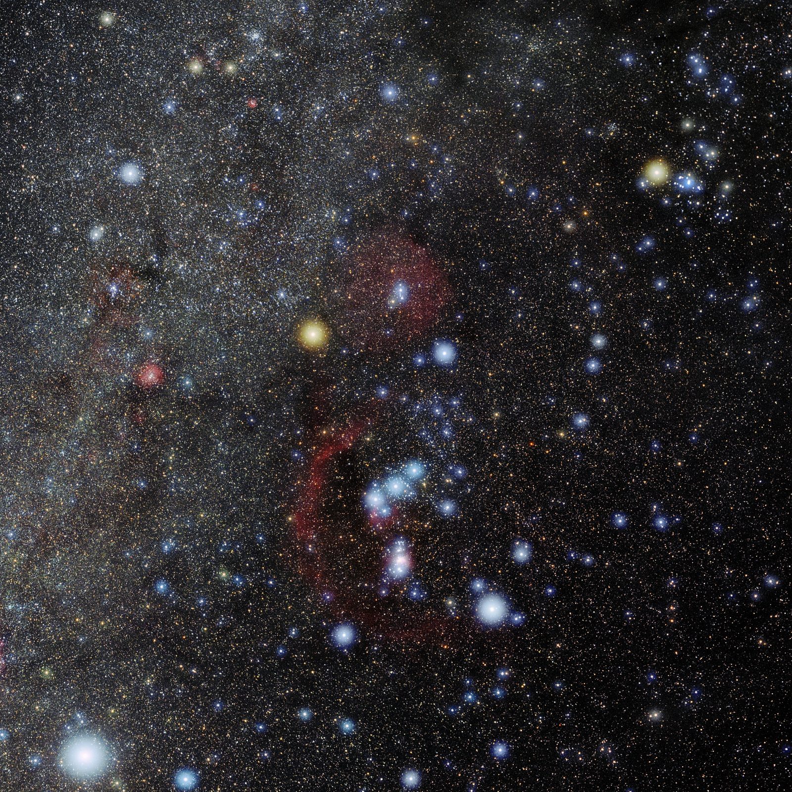 A square wide-field photograph of the constellation Orion on a near-black sky, the stars showing their colours. A large orange-red star sits at the upper left and a brilliant blue-white one at the lower right, with two fainter bright stars completing a long quadrilateral. Three stars in a short even row cross the middle, and below them hangs a small pink glow. Above the row, between the two upper stars, a faint small triangle of stars marks the head. Thousands of fainter stars fill the field behind.